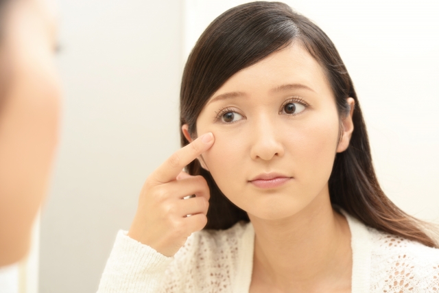 鏡を見ながら、目の下のシミに浮かない表情をする女性