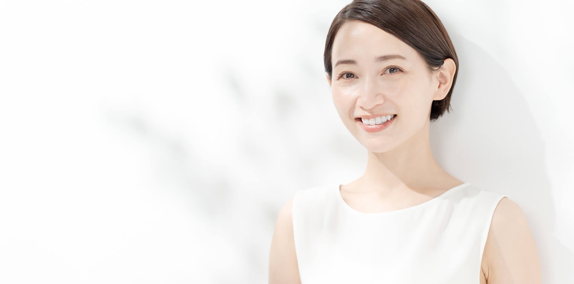 白い壁の前でショートカットの女性が見る人に笑顔を向けている画像