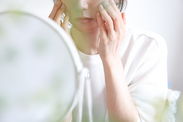 鏡を前にして両頬を抑える女性