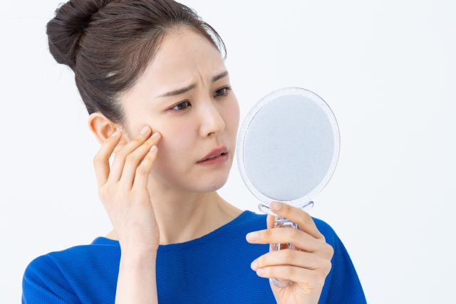 鏡を見て顔のシミを気にする女性