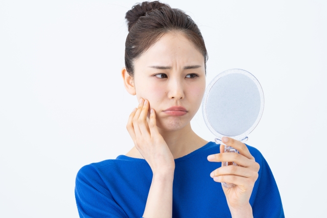 鏡を見ながら顔の悩みに不満そうな女性