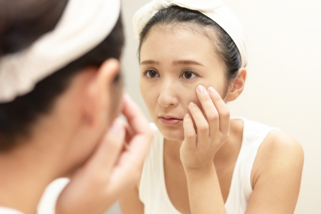 鏡を見ながら目元や頬のシミを気にする女性