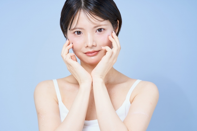 ショートカットの女性が水色の背景の前で両頬を触り微笑んでいる様子