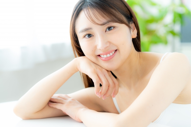 白いキャミソール姿の女性が頬杖ついて微笑んでいる様子